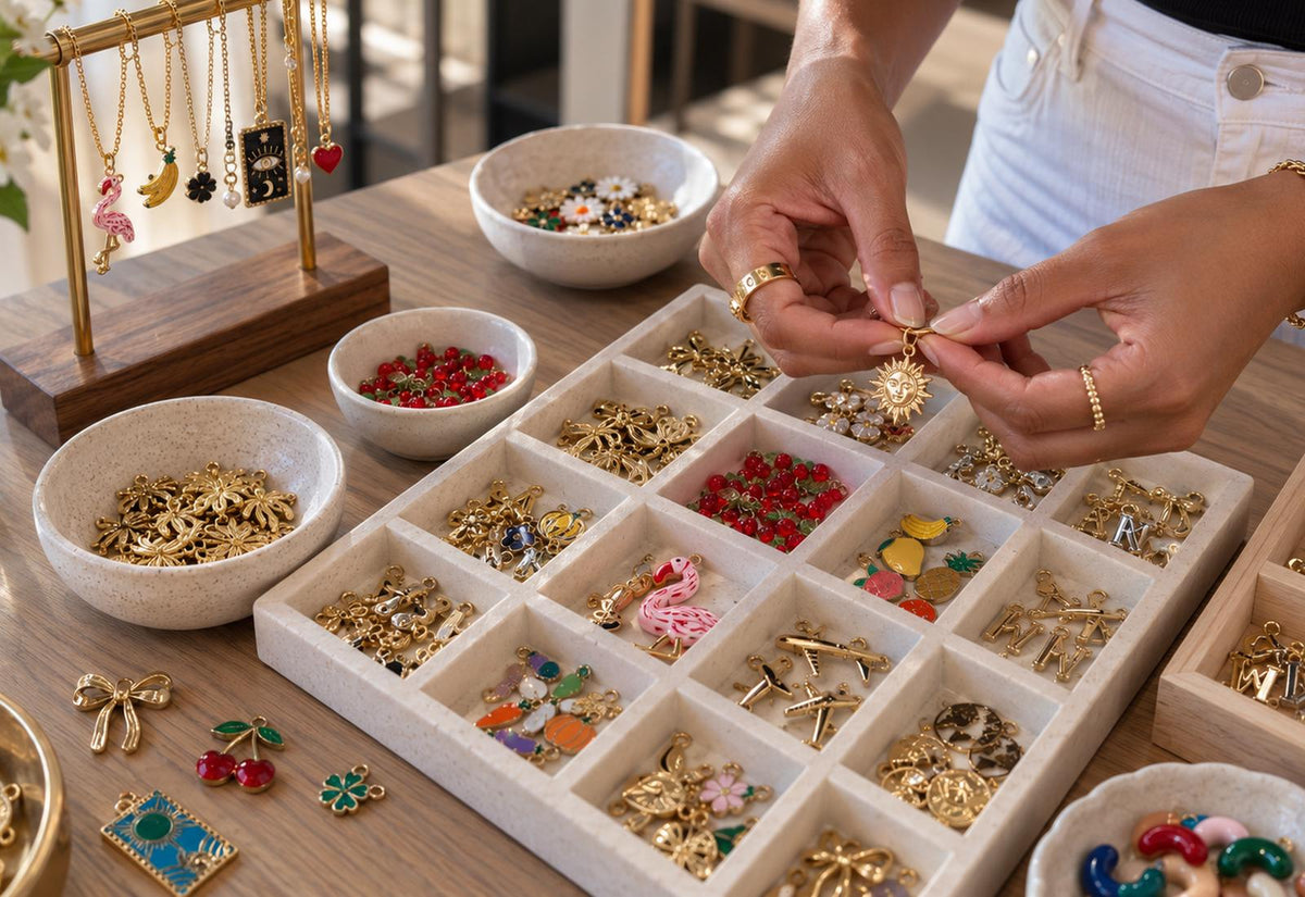 Hands attaching a gold sun charm over a tray of enamel and gold charms at the Covet Charm Bar