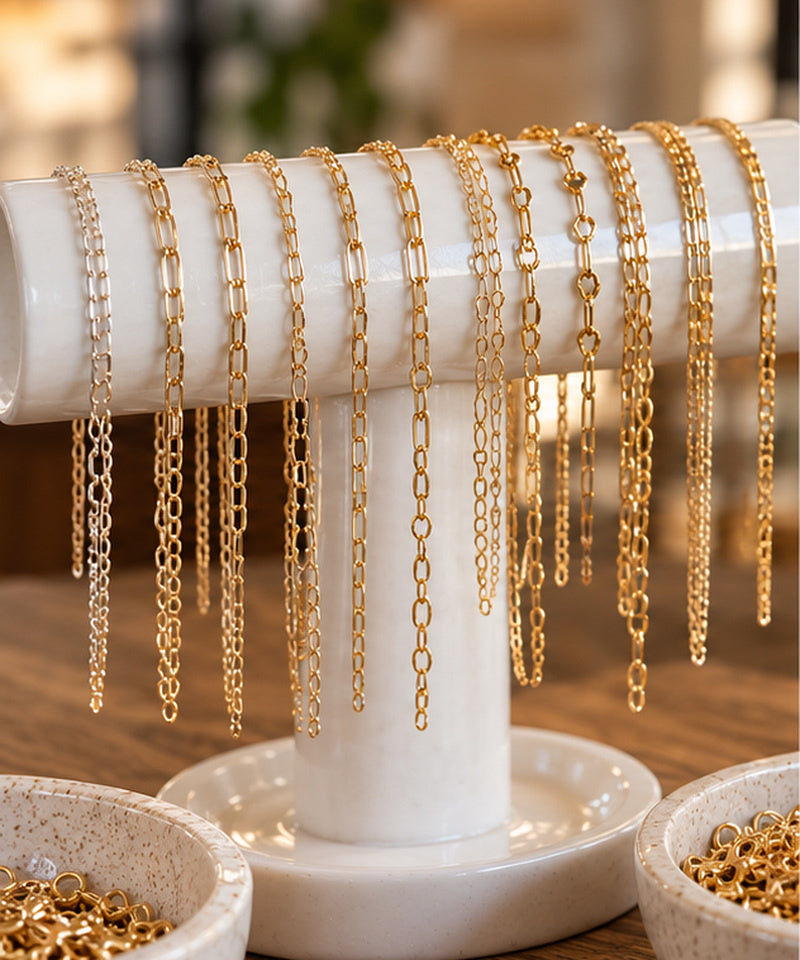 Gold and silver chain bracelets in a range of link styles on a white ceramic bar, with bowls of gold links on the table